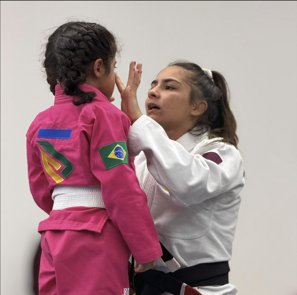 Female coach comforting a young girl in a pink gi during a girls-only Jiu Jitsu class in Doha